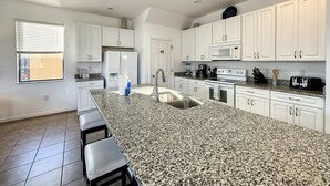 Een moderne keuken met witte kasten, een granieten aanrecht, roestvrijstalen apparatuur en een groot kookeiland met barkrukken.
