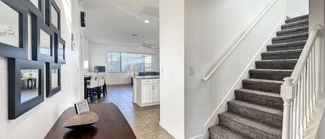 A spacious hallway with a wooden table, a staircase, and a kitchen area in the background.