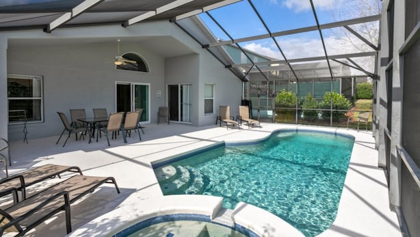 A modern outdoor pool area with a glass-enclosed roof, lounge chairs, and a clear view of the surrounding landscape.