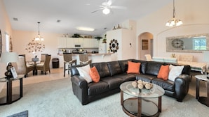 A modern living room with a black leather sofa, a glass coffee table, and a dining area with a chandelier.