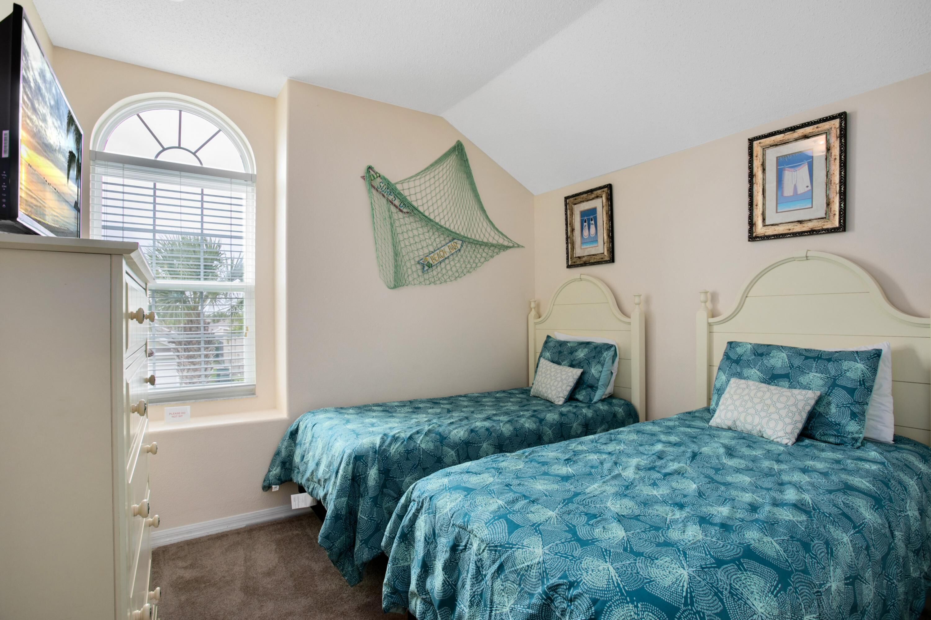A bedroom with two beds, a window with blinds, a green net on the wall, and a dresser.