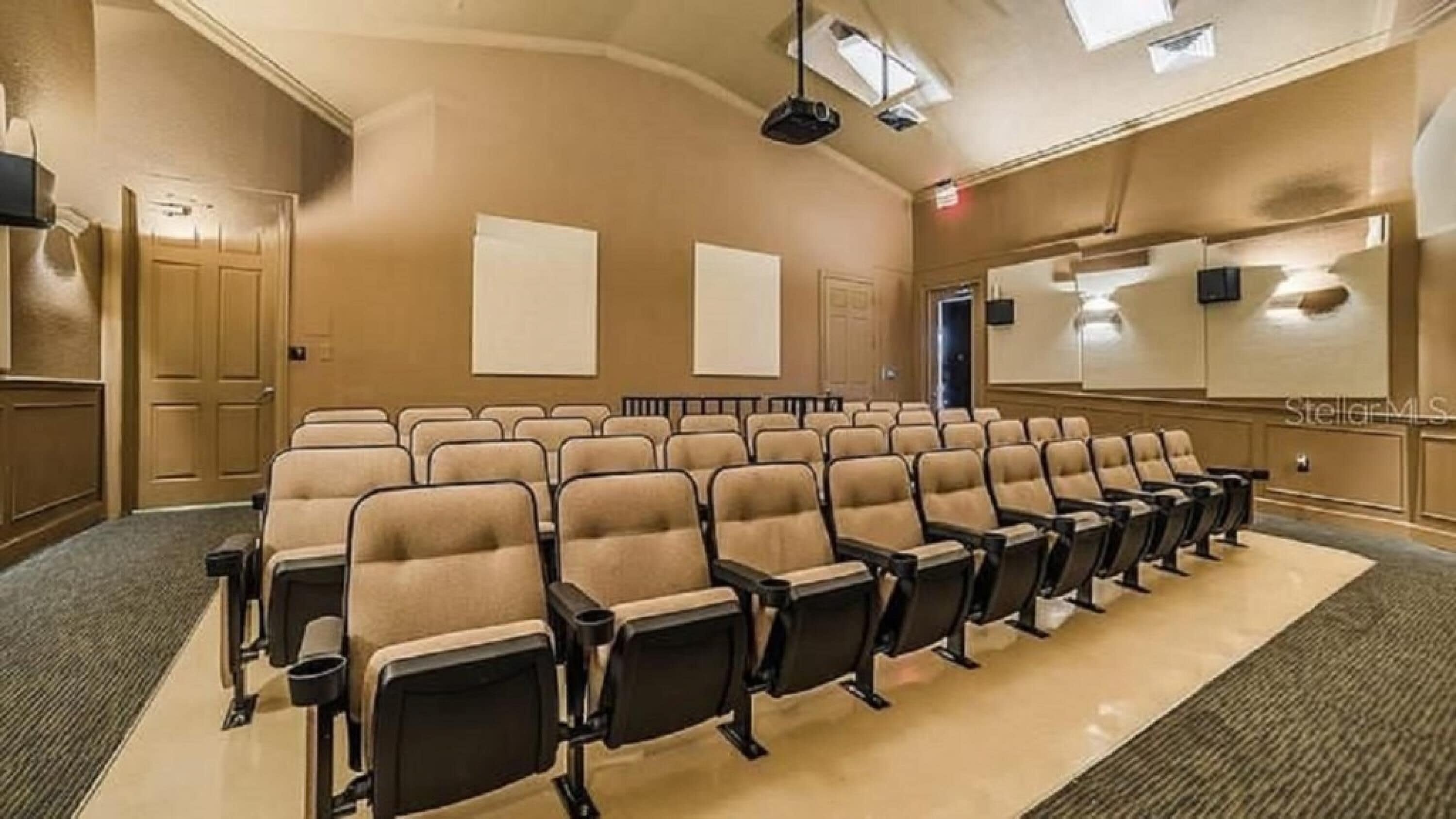 Ein Konferenzraum mit Reihen beige farbener Stühle, Teppichboden und einer Projektionsleinwand.