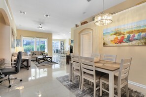 A spacious living room with a dining area, large windows, and a ceiling fan.