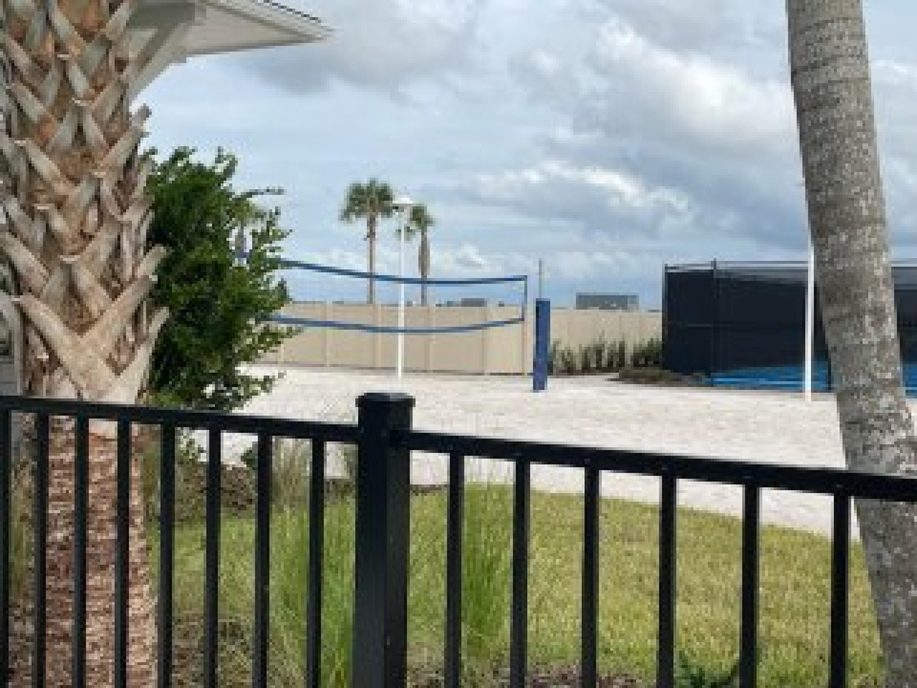 A fenced outdoor area with palm trees, a blue structure, and a building in the background.