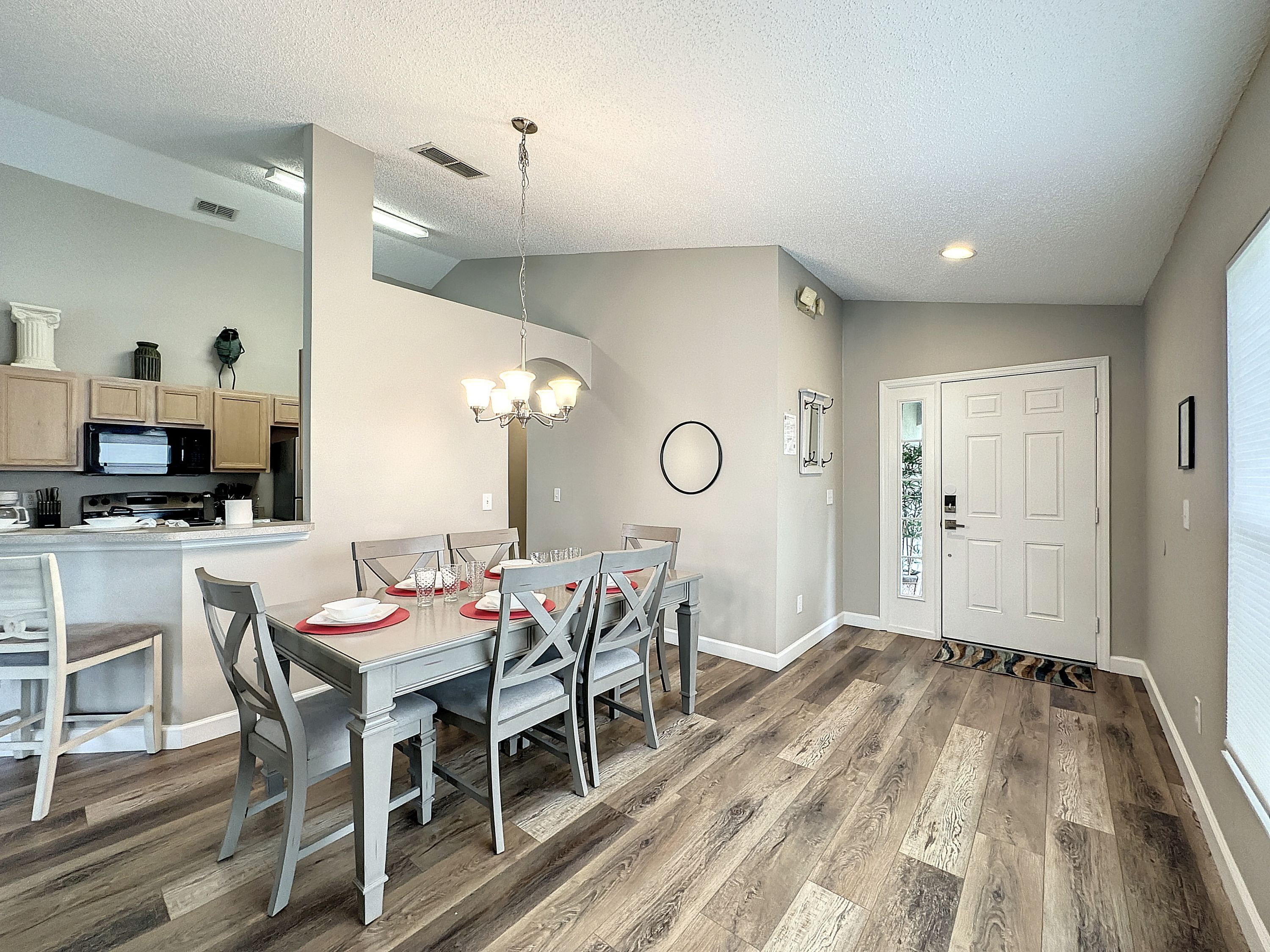 A dining area with a wooden floor, a chandelier, and a kitchen in the background.