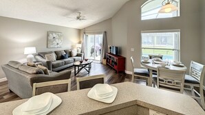 A spacious living room with a grey sofa, a coffee table, and a dining area with a table and chairs. - 4 Bed 3 Bath in a Gated Community With Pool (Kissimmee)