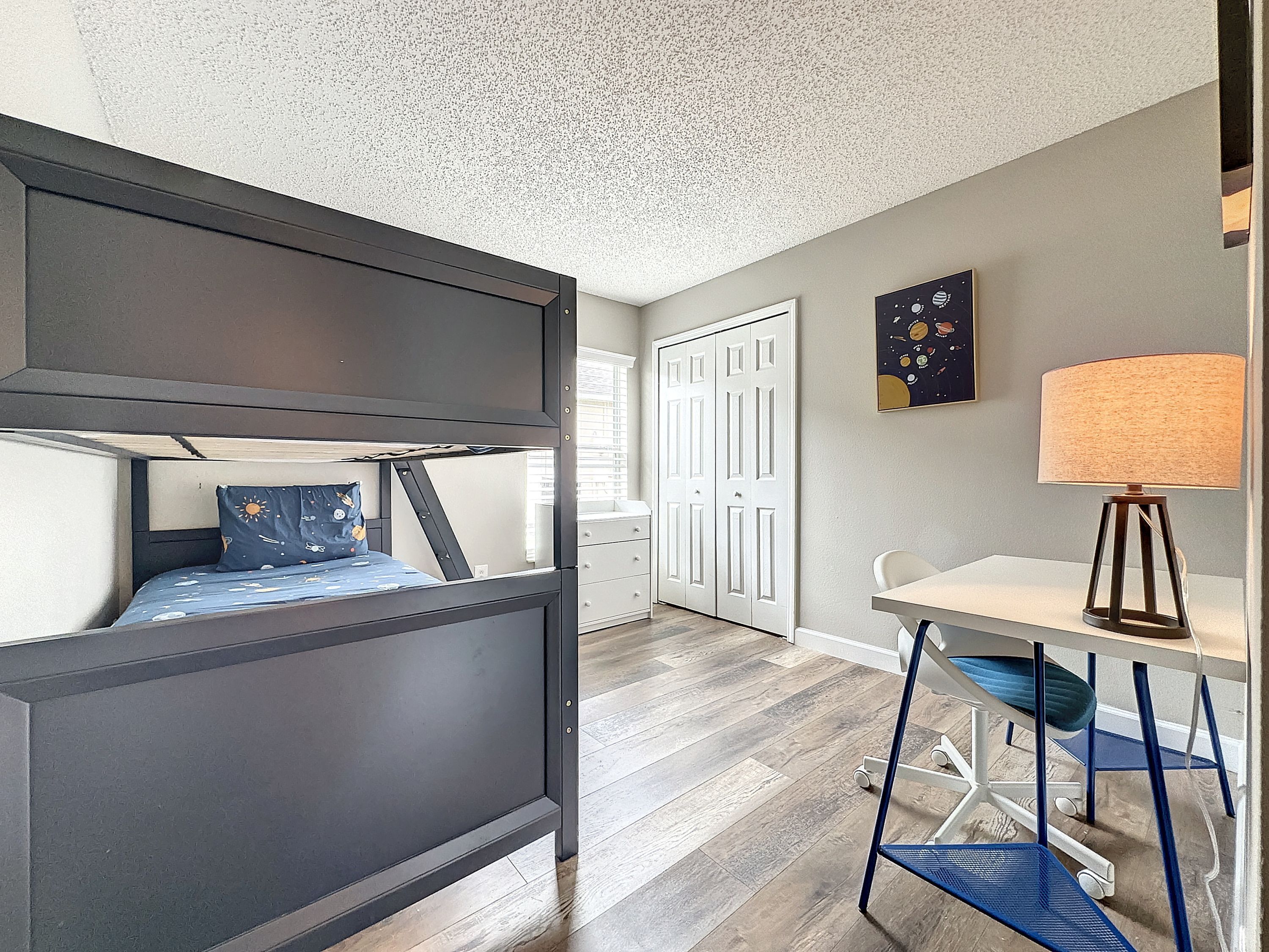 A bedroom with a bunk bed, a desk, a chair, and a lamp.