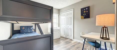 A bedroom with a bunk bed, a desk, a chair, and a lamp.
