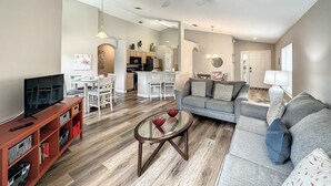 A spacious living room with a grey sofa, a coffee table, and a TV stand. There is a dining area with chairs and a table, and a kitchen in the background. - 4 Bed 3 Bath in a Gated Community With Pool (Kissimmee)