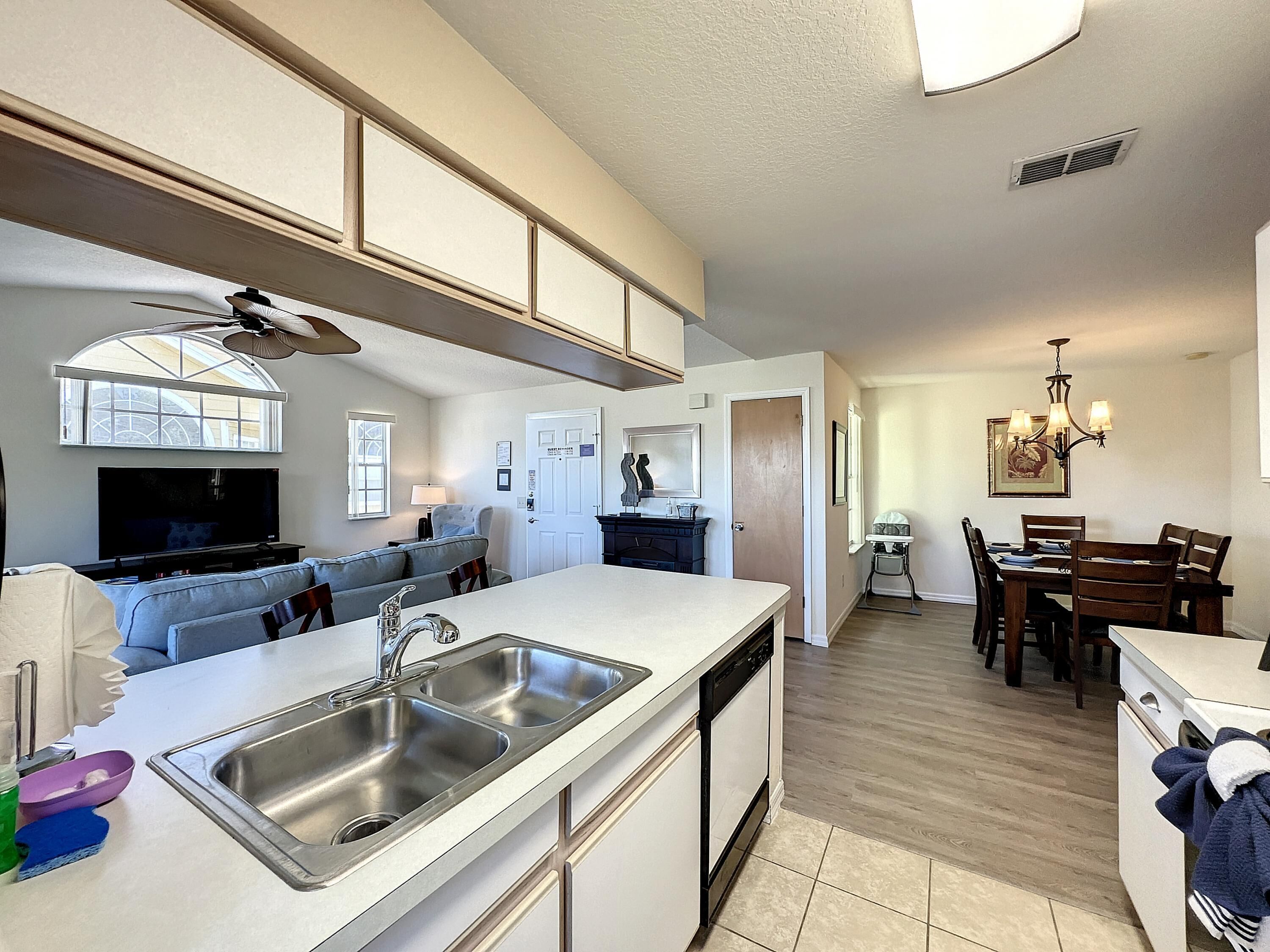 A modern kitchen with a large island, built-in dishwasher, and a dining area with wooden chairs and a chandelier.