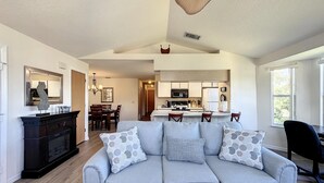 A living room with a grey sofa, a dining area with wooden chairs, a kitchen with a microwave, and a large window. - Lovely 3 bed Condo Near Disney Quiet Community (Kissimmee)