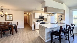 A modern kitchen with a central island, wooden dining table, and chairs. - Lovely 3 bed Condo Near Disney Quiet Community (Kissimmee)