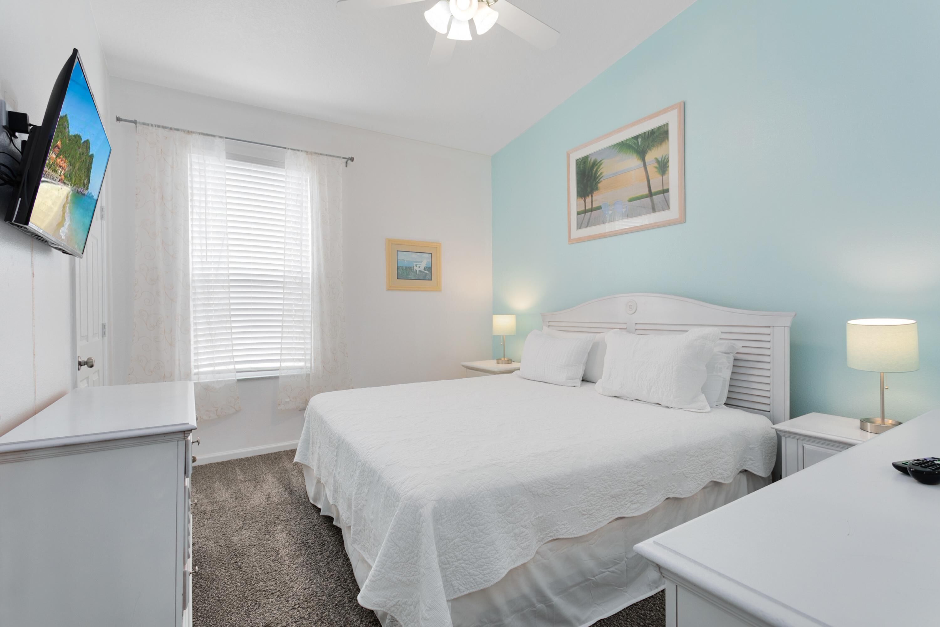 A bedroom with a bed, bedside tables, a TV mounted on the wall, and a window with curtains.