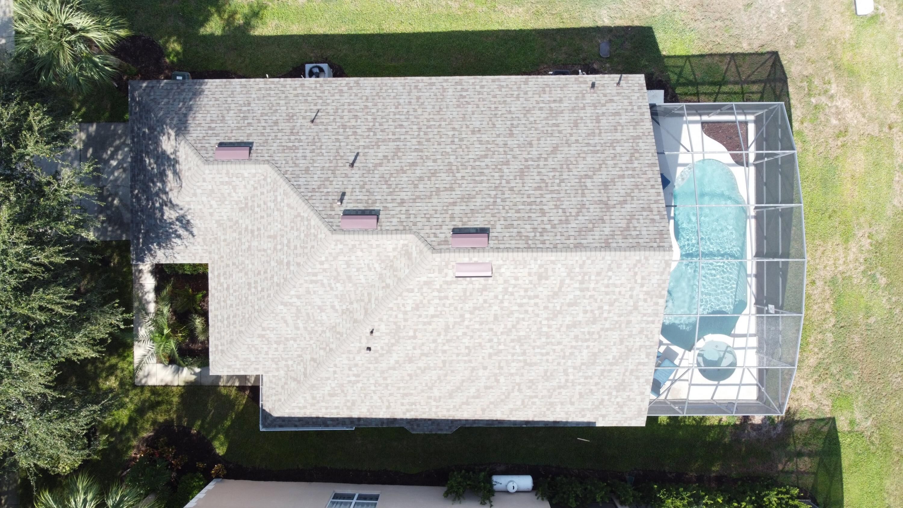 An aerial view of a house with a large roof, a swimming pool, and surrounding greenery.