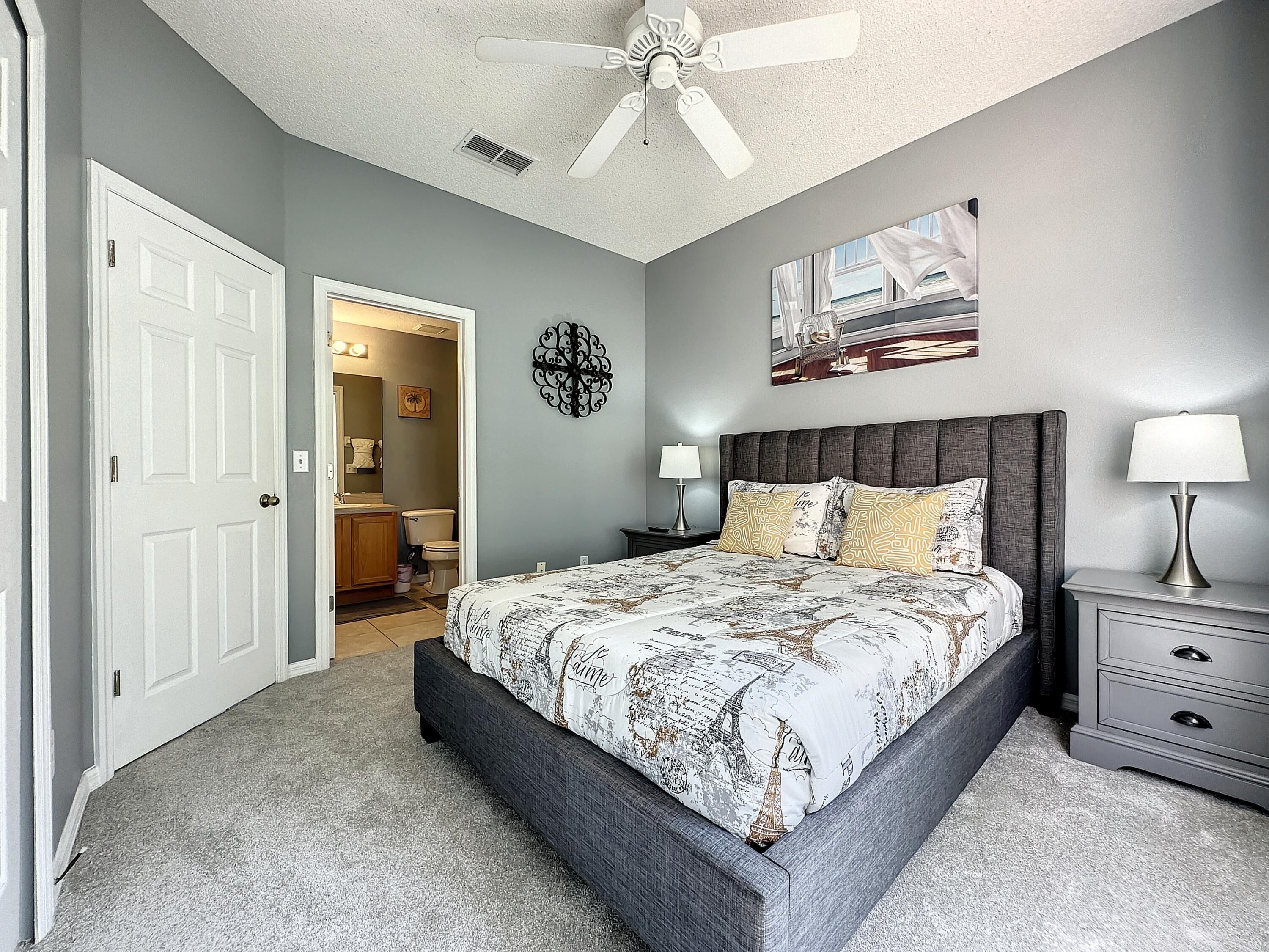 A bedroom with a bed, nightstands, a ceiling fan, and a bathroom visible through an open door.