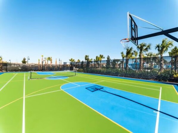 Un terrain de basket en plein air, avec un ciel dégagé et des palmiers en arrière-plan.