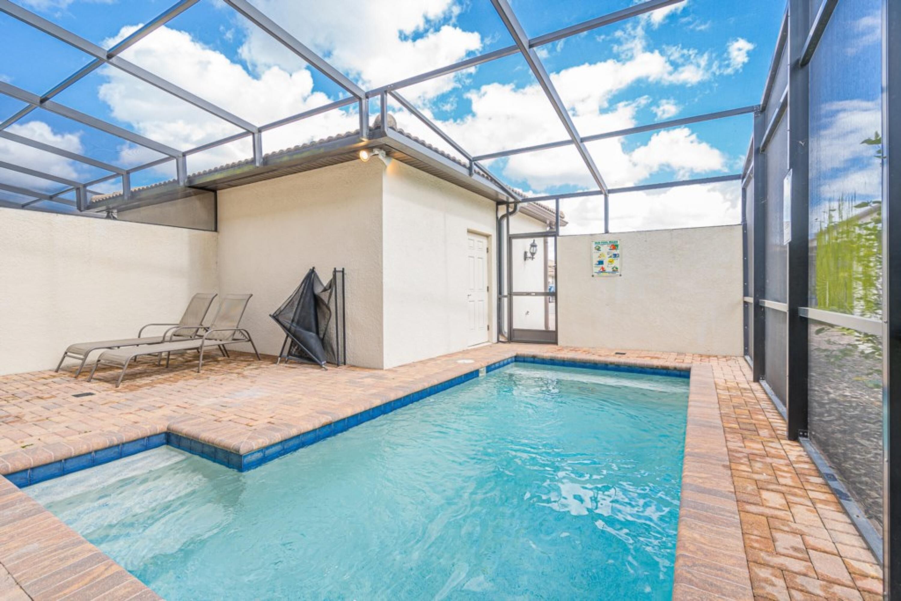 An indoor swimming pool with a tiled floor, a glass ceiling, and a door leading to another room.