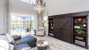 A spacious living room with a large sectional sofa, a chandelier, a fireplace, and a view of a swimming pool. - 5 Bedroom Home is Ideal for an Elegant Vacation (Kissimmee)