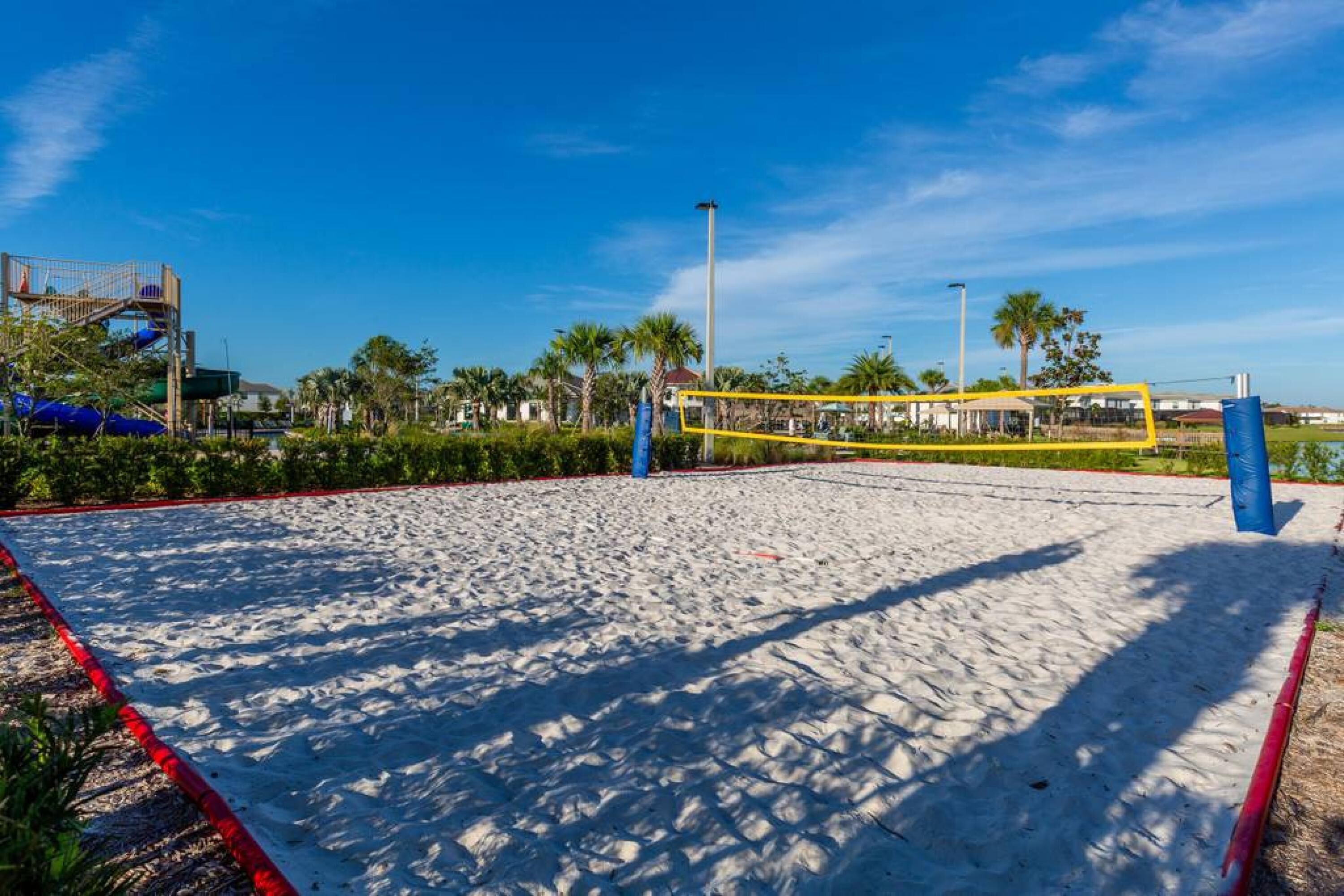 Ein Sandvolleyballfeld mit Netz, umgeben von Palmen und blauem Himmel.