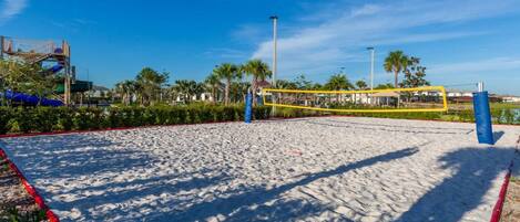 Ein Sandvolleyballfeld mit Netz, umgeben von Palmen und blauem Himmel.