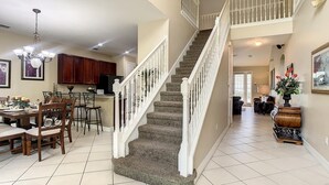 A spacious kitchen with dark granite countertops, a dining area with wooden chairs, and a staircase with white railings. - Fantastic 7 Bed 6 Bath in Prestigious Gated Comm (Kissimmee)