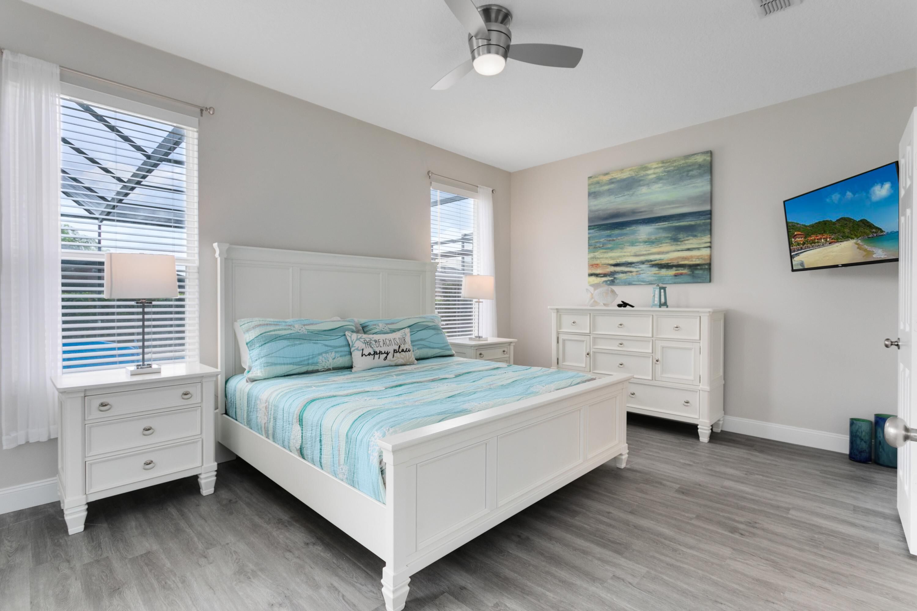 A bedroom with a white bed, a nightstand, a dresser, and a ceiling fan.