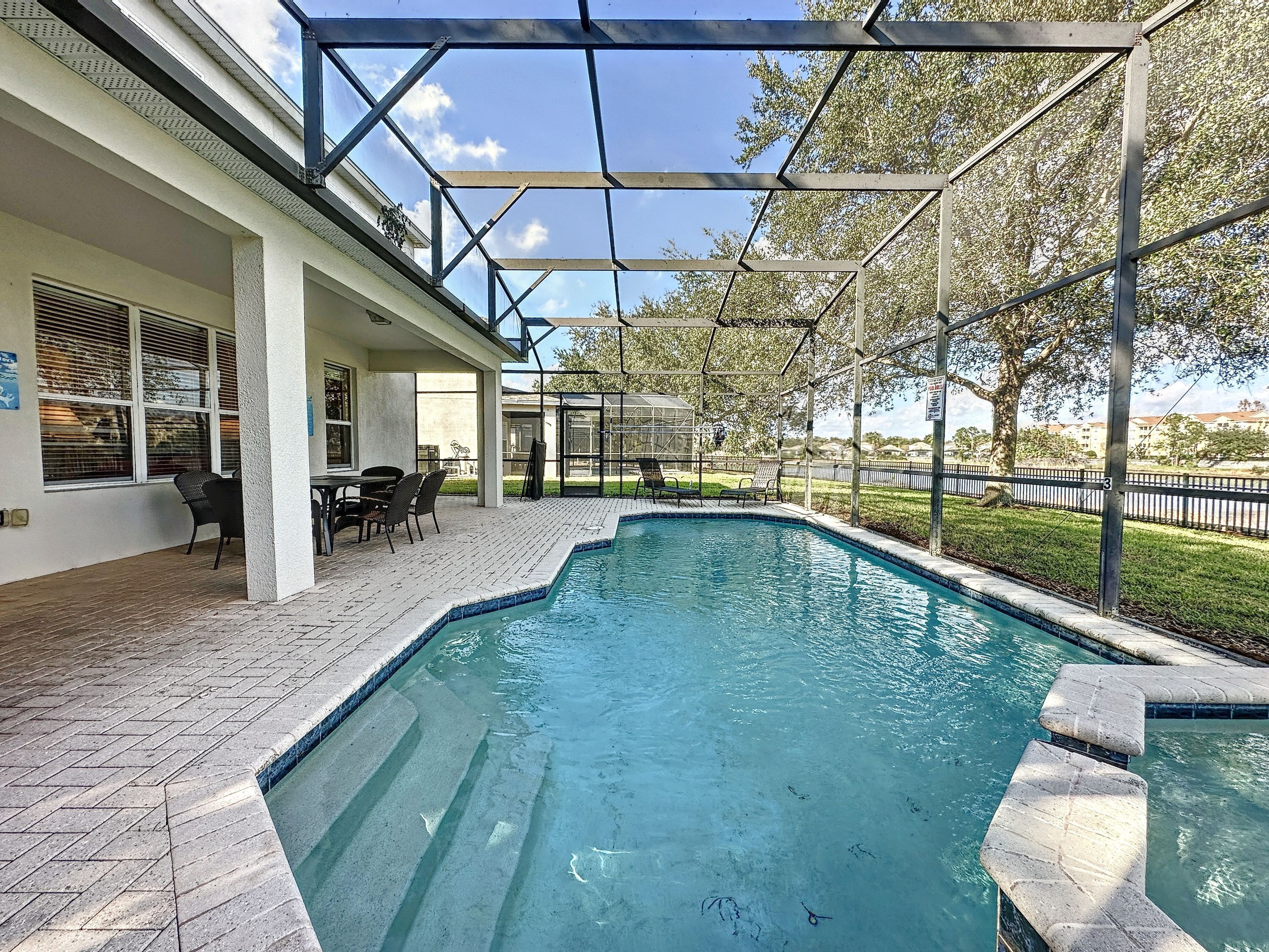 Uma piscina com um terraço coberto, área de estar externa e vista da paisagem ao redor.