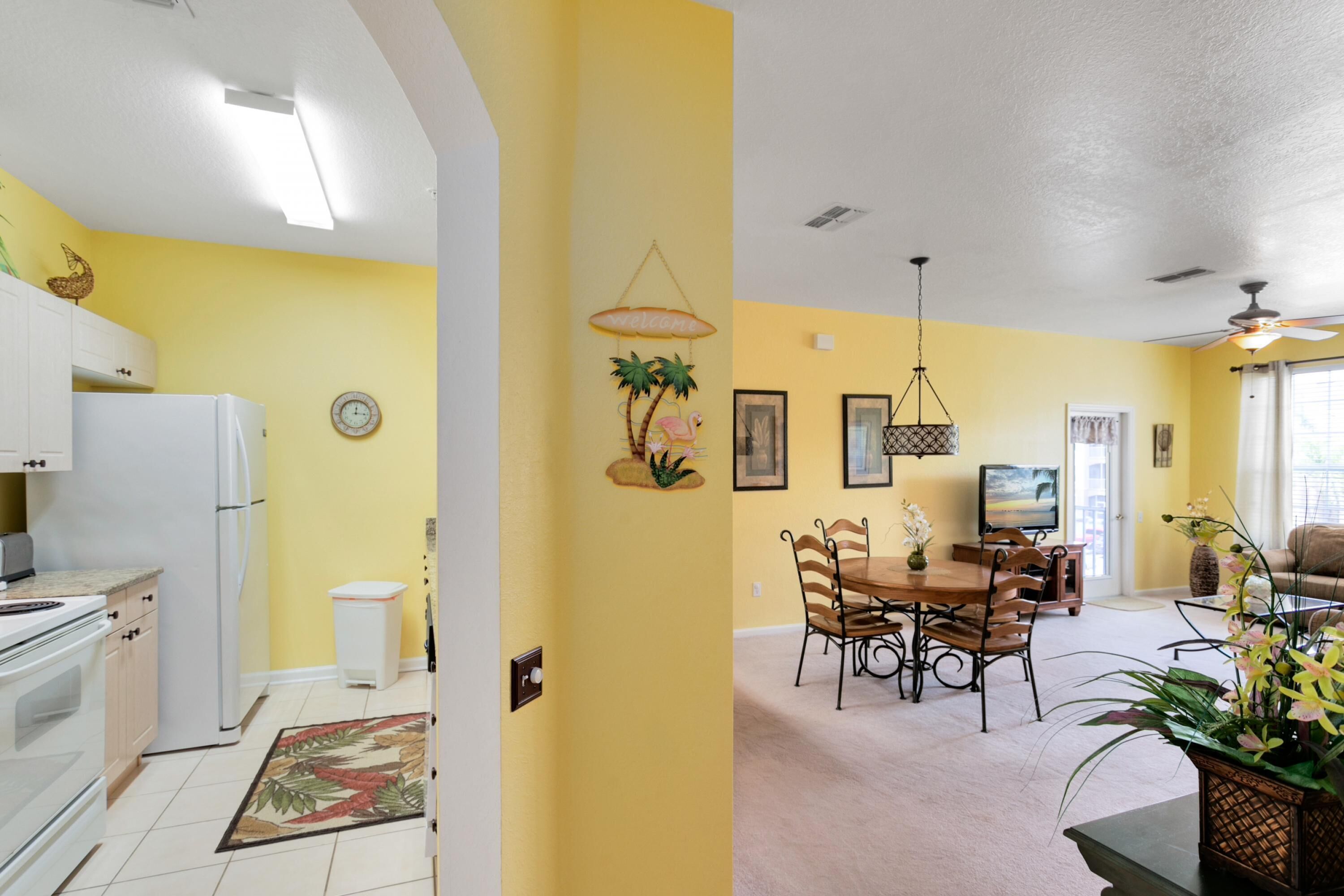 A kitchen with white appliances, a dining area with a wooden table and chairs, and a living room with a sofa and a TV.