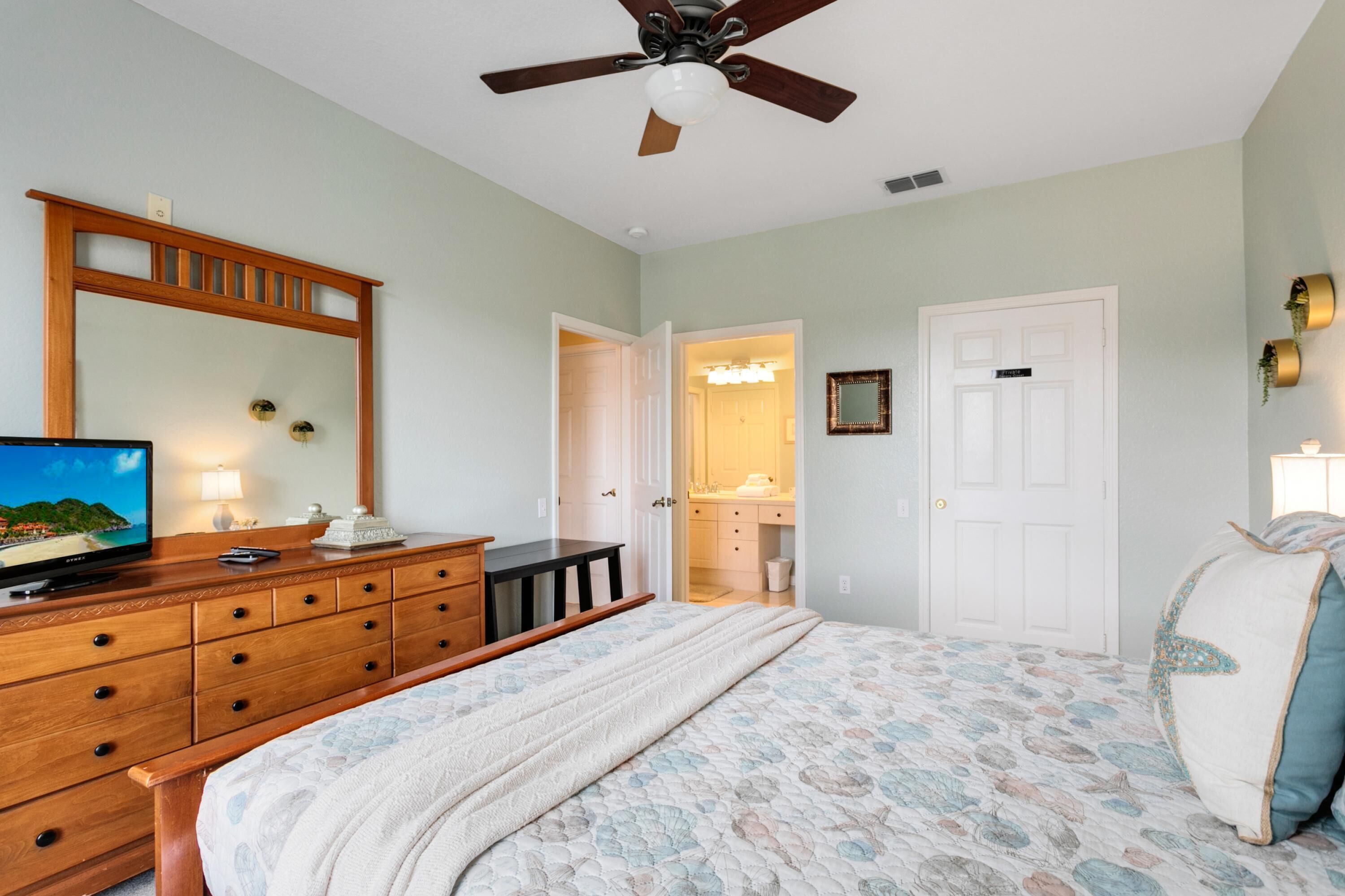 Une chambre à coucher comprenant un lit, une commode, un téléviseur et un ventilateur de plafond.