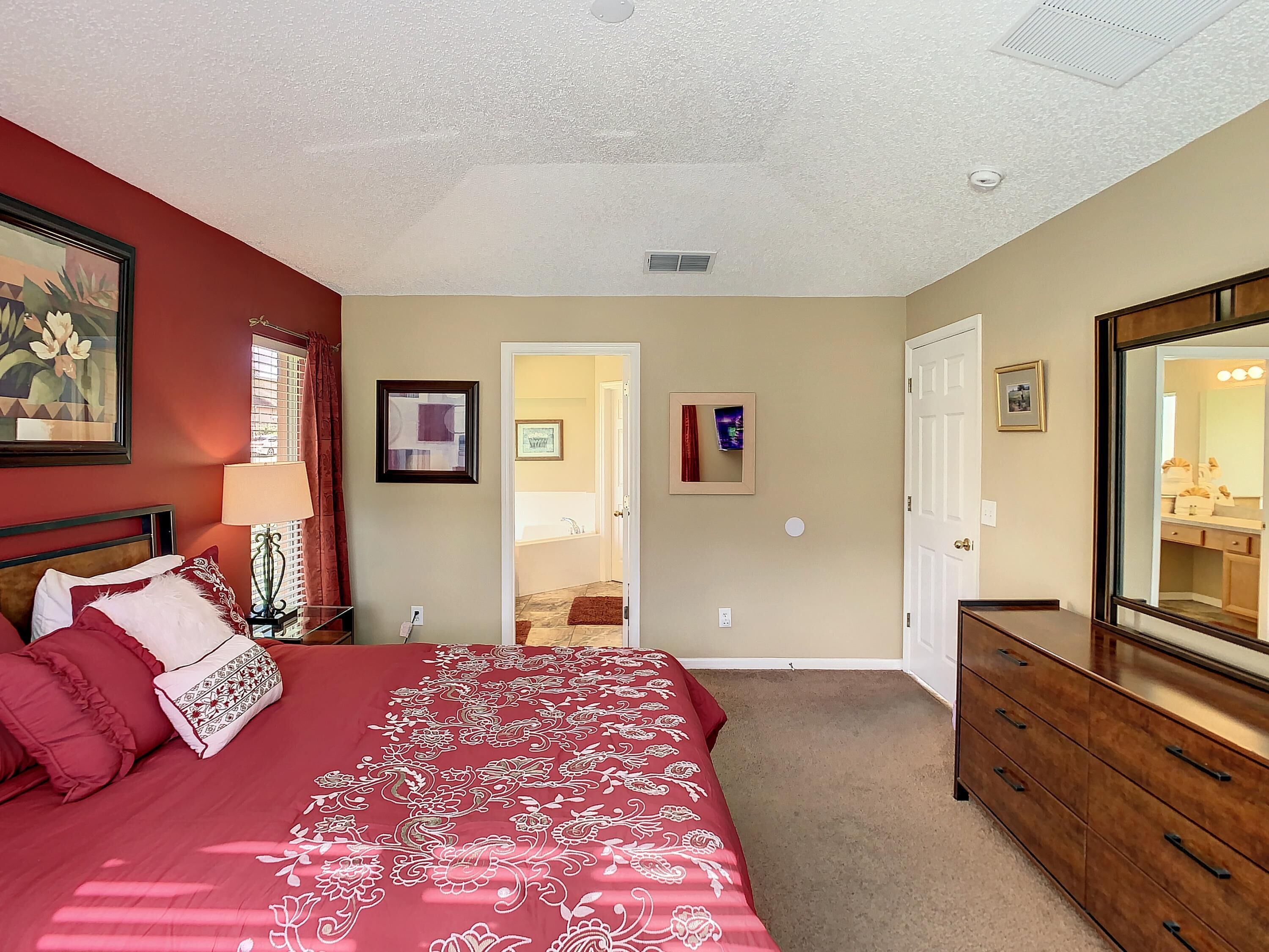 A bedroom with a large bed, a dresser, a mirror, and a door leading to a bathroom.