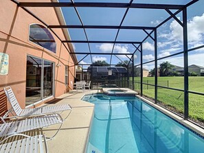 A swimming pool with a glass enclosure, white lounge chairs, and a patio area with a table and chairs. - Emerald Island Resort 4 bed 3 Bath With Pool spa (Kissimmee)