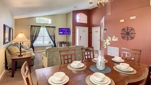 A dining area with a wooden table set for four, a chandelier, and a television in the background. - Emerald Island Resort 4 bed 3 Bath With Pool spa (Kissimmee)