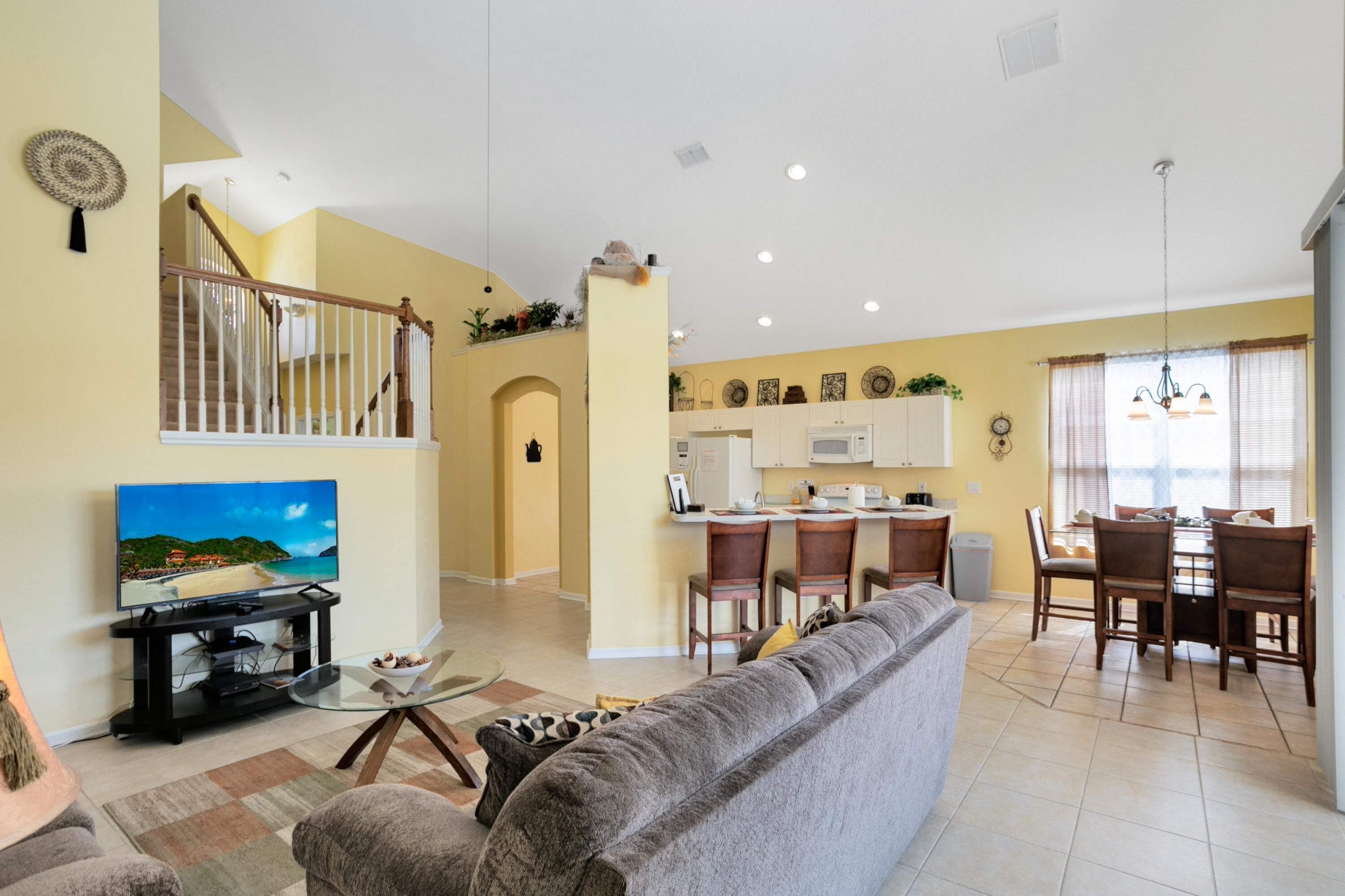 A spacious living room with a large gray sofa, a flat-screen TV, and a dining area with wooden chairs and a table.