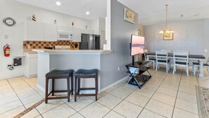A modern kitchen with white cabinets, a central island, and a dining area with a table and chairs. - 3Br 2Ba Private Pool Villa Just Steps Away From (Kissimmee)