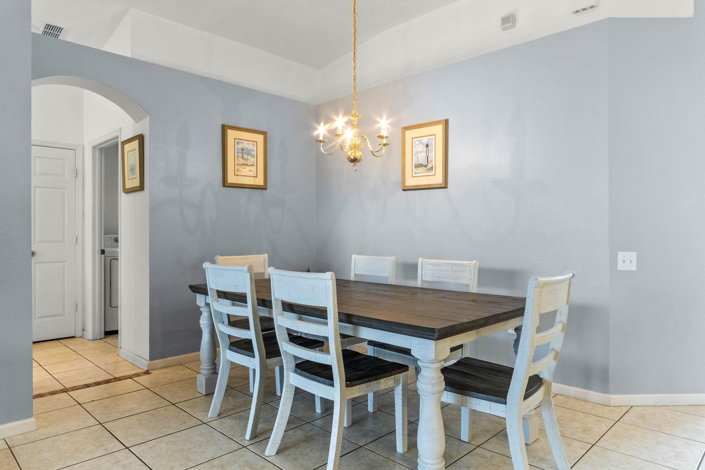 A dining area with a wooden table and white chairs, a chandelier, and framed pictures on the wall.