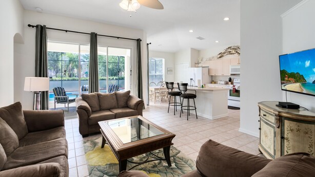 A spacious living room with a large window, a ceiling fan, and a television on a cabinet. - 4 Bedroom 3 Bath South Facing Pool Spa Villa (Kissimmee)