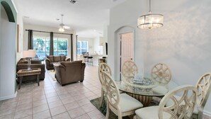 A spacious living area with a dining table and chairs, a sofa set, and a large window providing natural light. - 4 Bedroom 3 Bath South Facing Pool Spa Villa (Kissimmee)