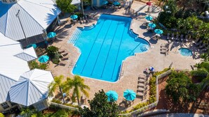 A large swimming pool with multiple lanes, surrounded by lounge chairs and umbrellas, and adjacent to a building with a distinctive roof. - 4 Bedroom 3 Bath South Facing Pool Spa Villa (Kissimmee)