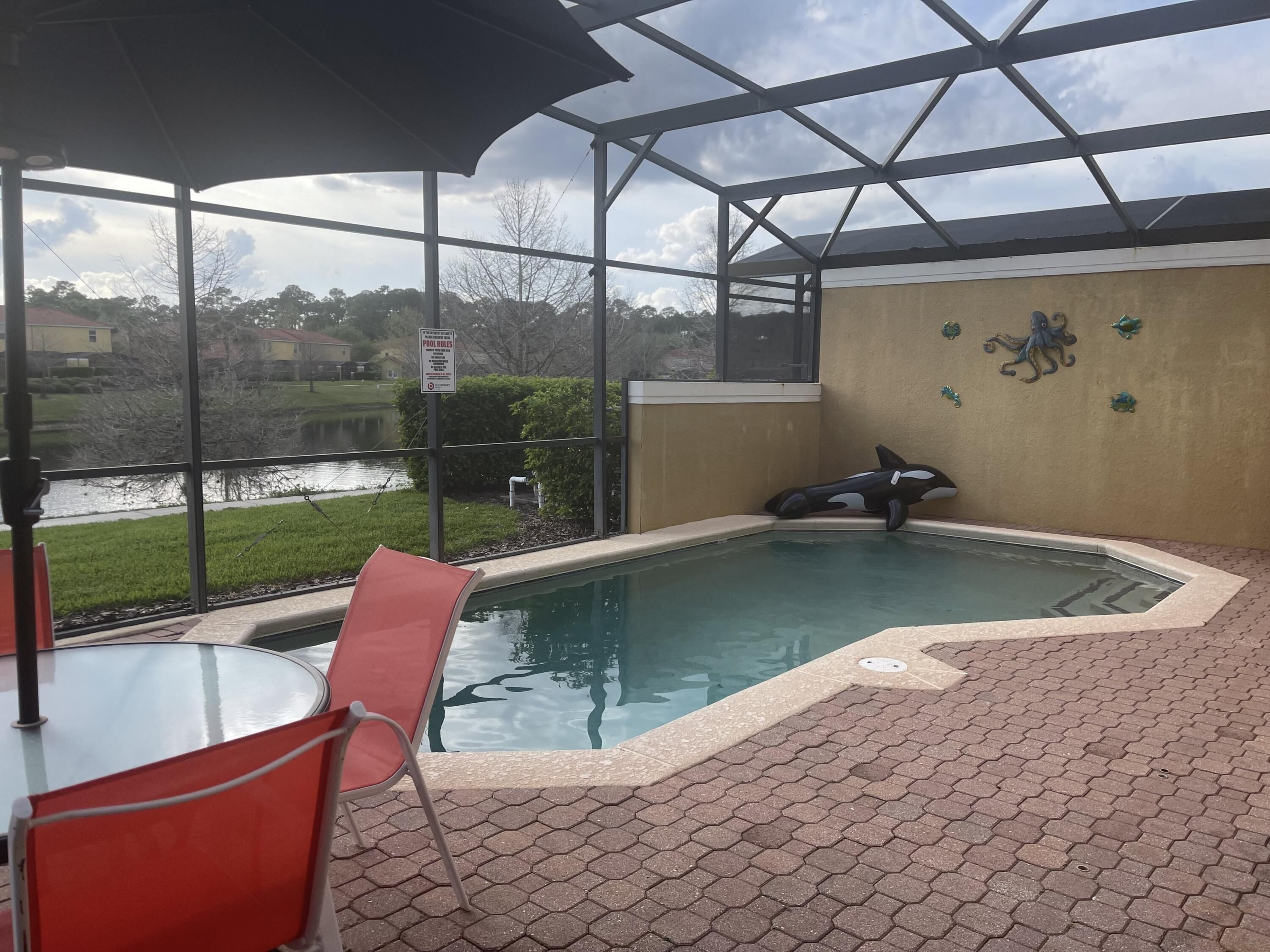A covered outdoor pool area with a view of a lake, a red chair, and a pool rule sign.