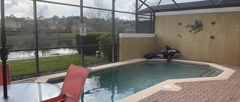 A covered outdoor pool area with a view of a lake, a red chair, and a pool rule sign.