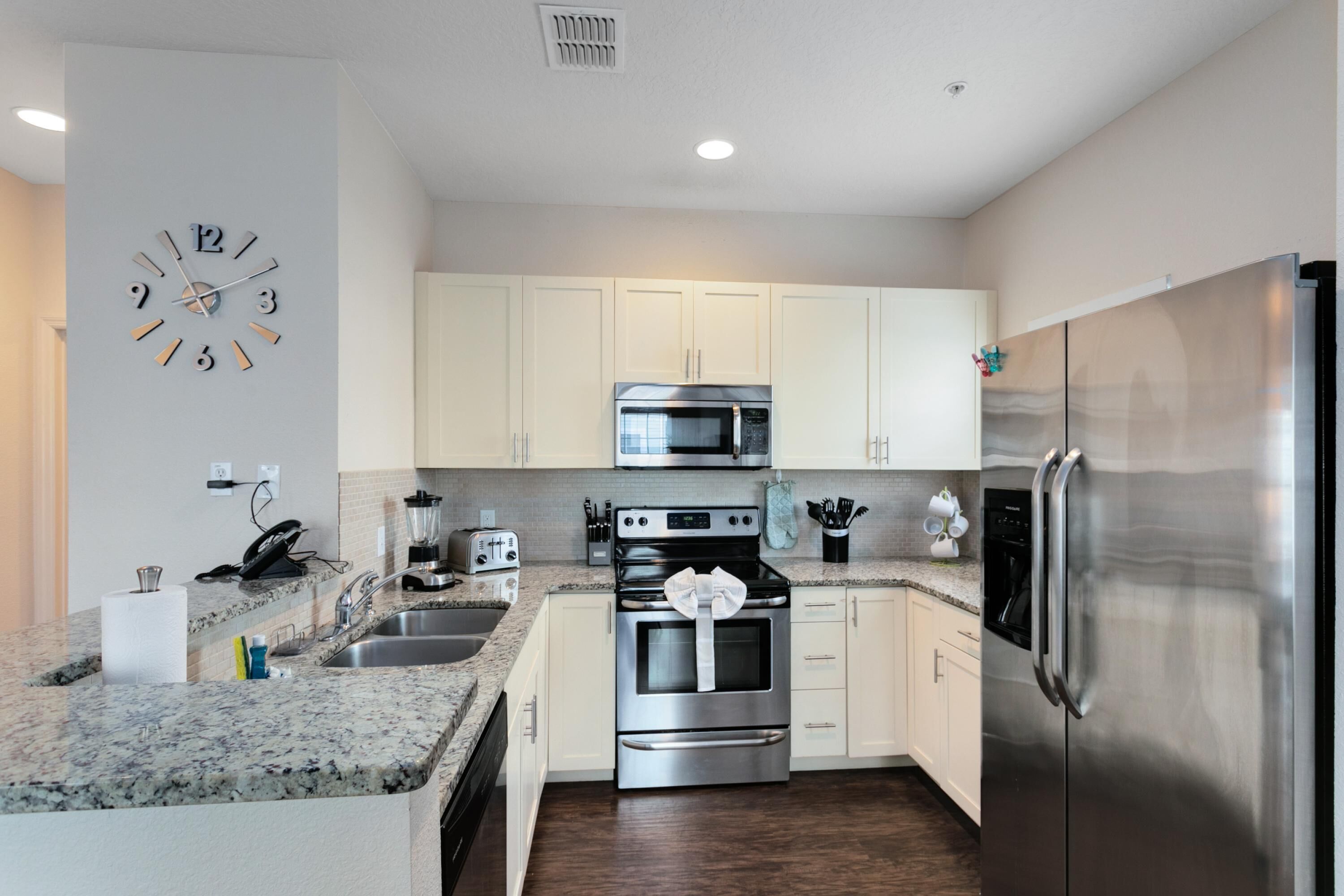 Una cocina moderna con armarios blancos, electrodomésticos de acero inoxidable, una encimera de granito y un reloj de pared.