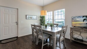 A dining area with a table, chairs, a TV, and a window with blinds. - Lucaya Village Resort - 4 Bed 3 Bath Townhouse (Kissimmee)