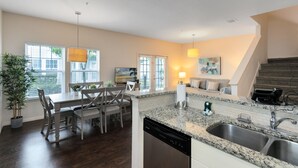 A modern kitchen with a granite countertop, stainless steel sink, and a dishwasher. There is a dining area with a table and chairs, and a staircase leading to another level. - Lucaya Village Resort - 4 Bed 3 Bath Townhouse (Kissimmee)