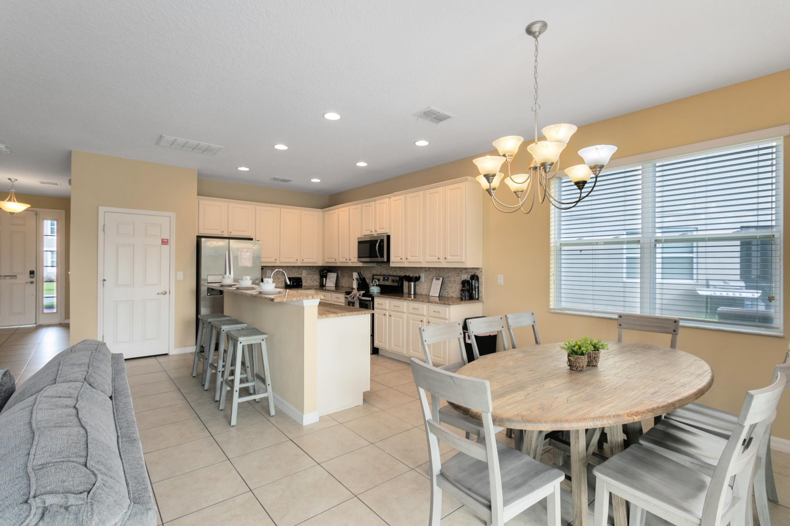 A modern kitchen with white cabinets, a central island, and a dining area with a wooden table and white chairs.