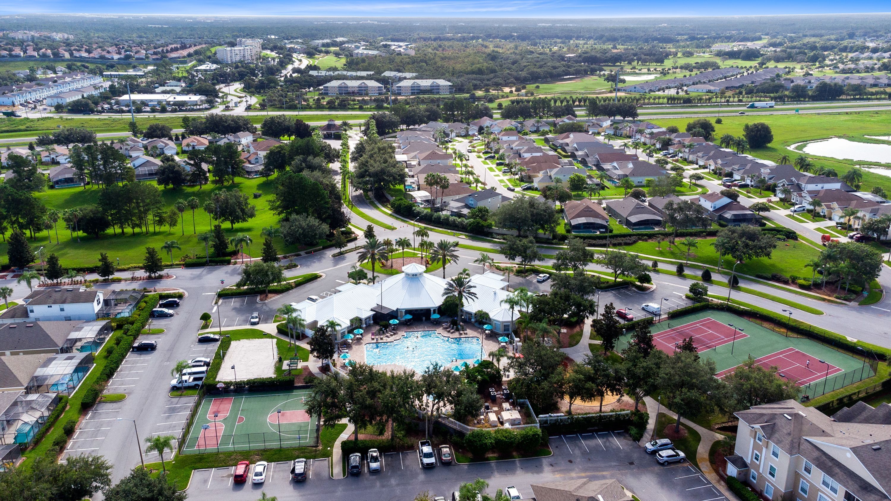 An aerial view of a residential area with a swimming pool, tennis courts, and a parking lot.