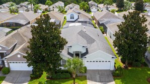 Un quartier résidentiel où les maisons se distinguent par leurs toits inclinés, avec une maison blanche au centre dotée d’un garage, le tout entouré de verdure.