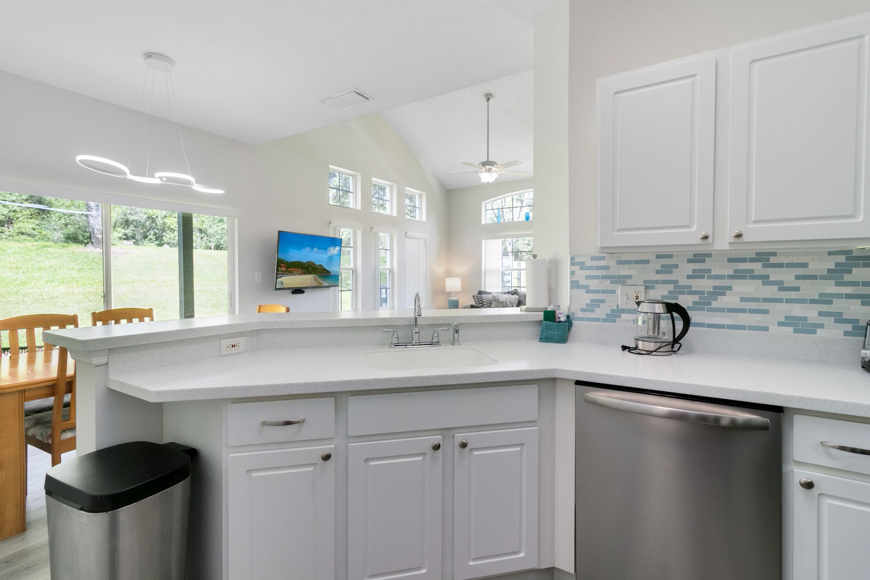 A modern kitchen with white cabinetry, a stainless steel dishwasher, and a tiled backsplash.