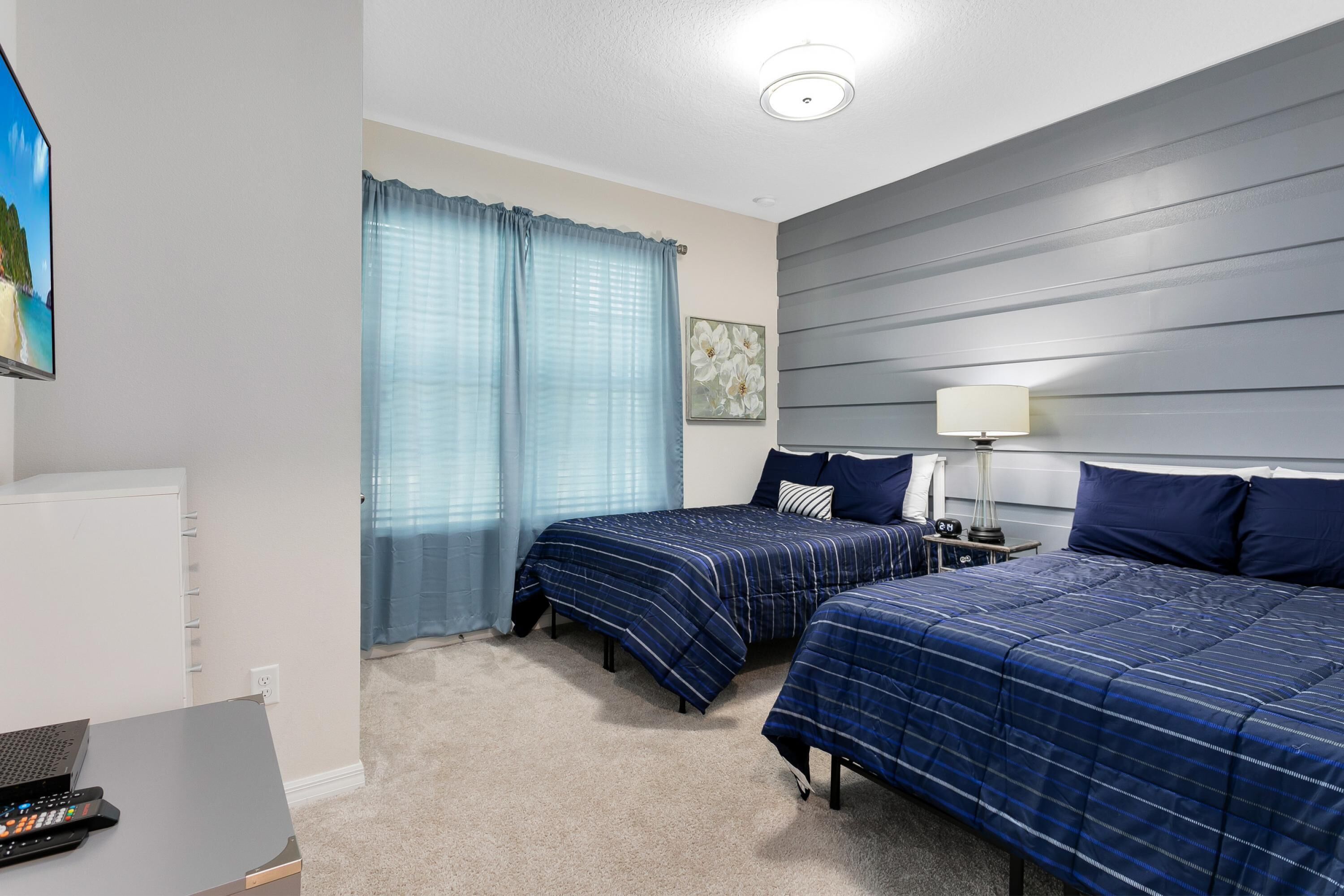 A hotel room with two beds, a desk, a lamp, and a painting on the wall.