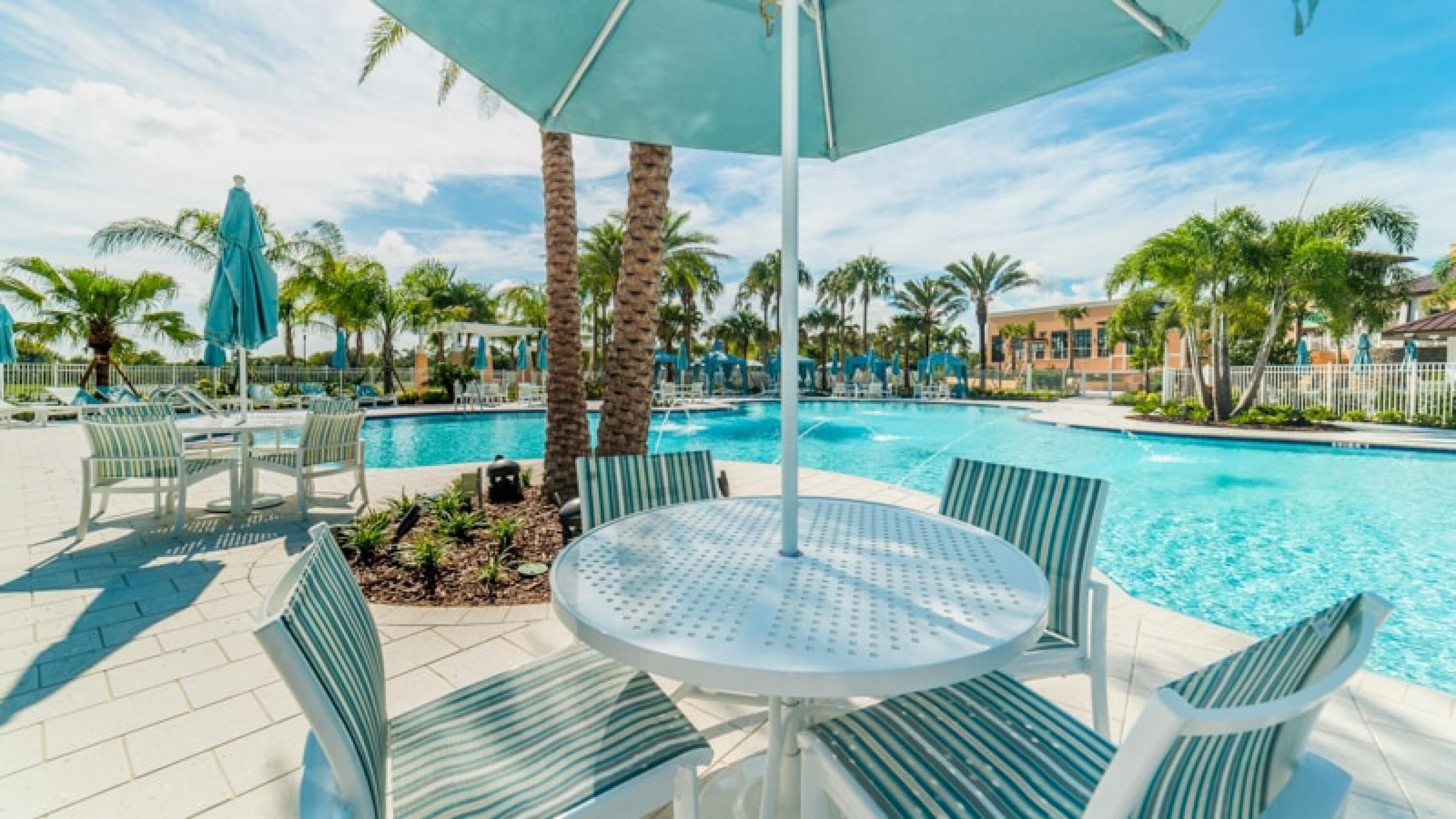 A pool area with lounge chairs, a round table, and umbrellas.
