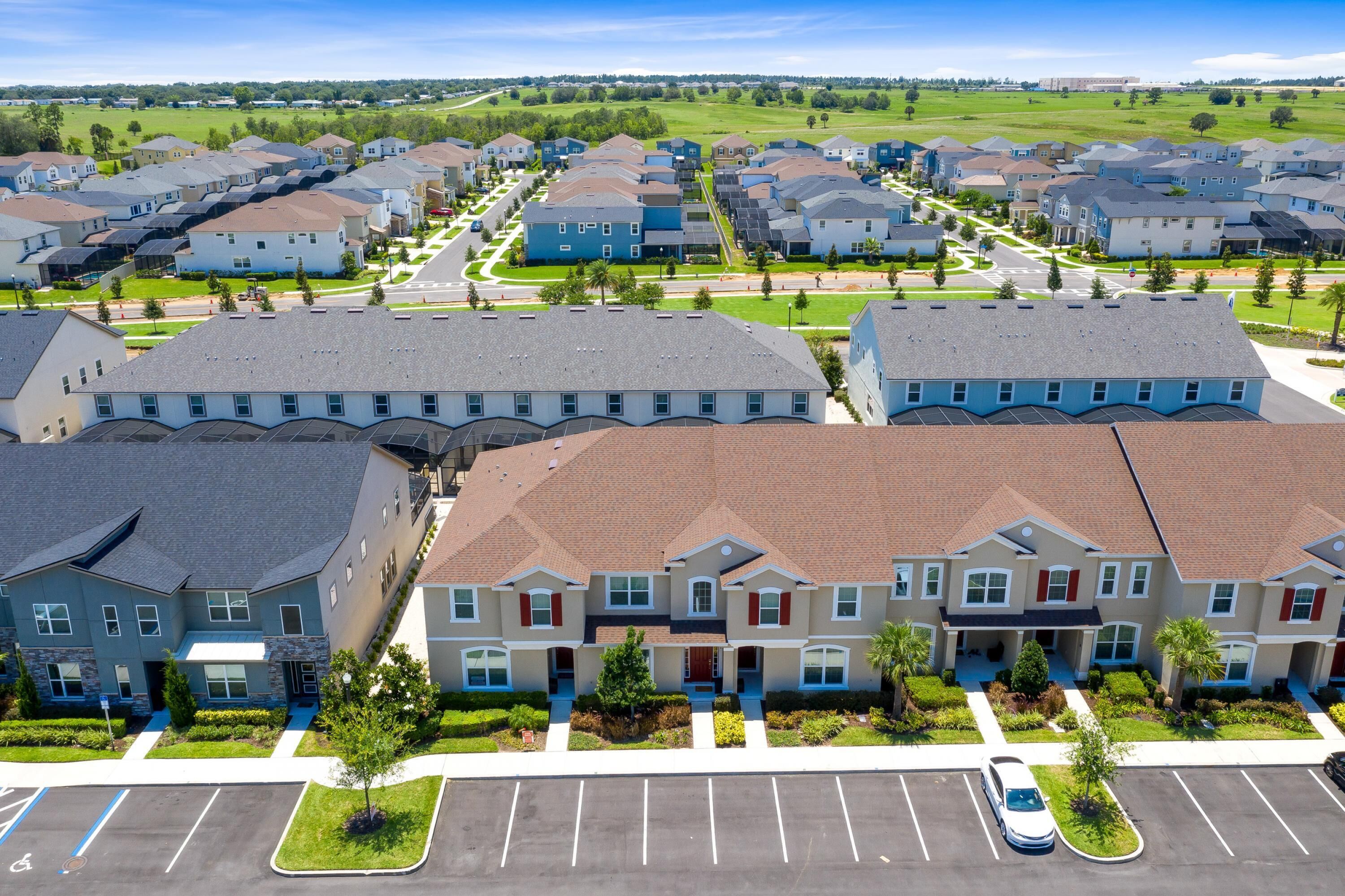 A residential area with modern two-story houses, a parking lot, and a clear sky.